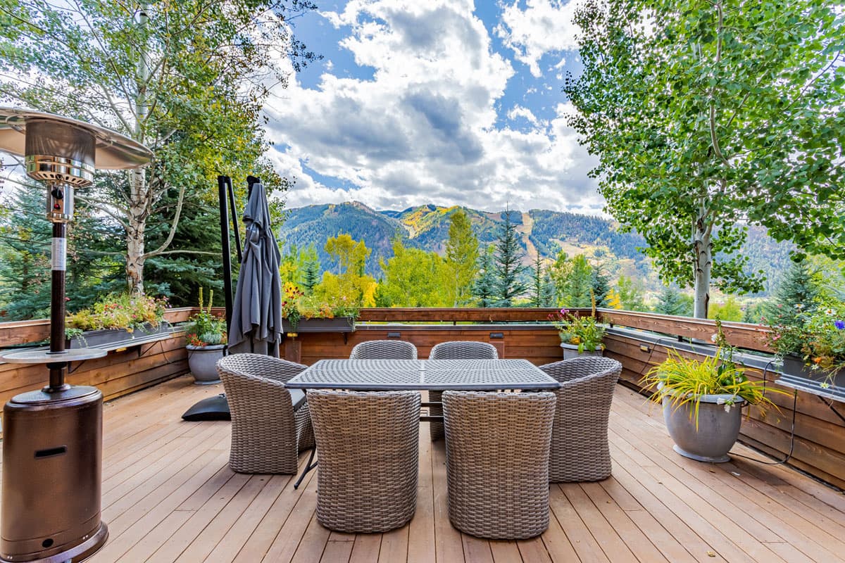 Outdoor wooden patio with a dining space, nearby tall trees and a look out into the outdoors in Aspen, Colorado.