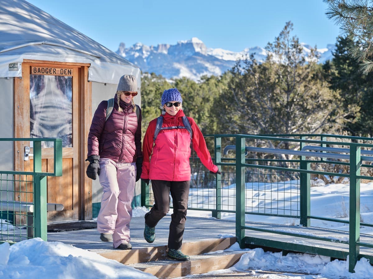 Two people walk out of a yurt into a snowy landscape in Ridgway