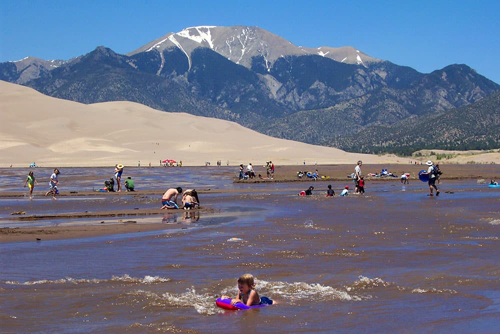 People splash in the water running through the sand at Great Sand Dunes National Park in summer