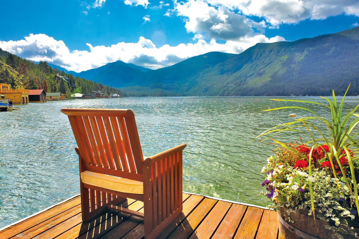 A chair sits on a dock overlooking a beautiful lake and mountains