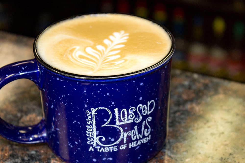 A milky latte in a dark blue mug from Blessed Brews Coffee Shop