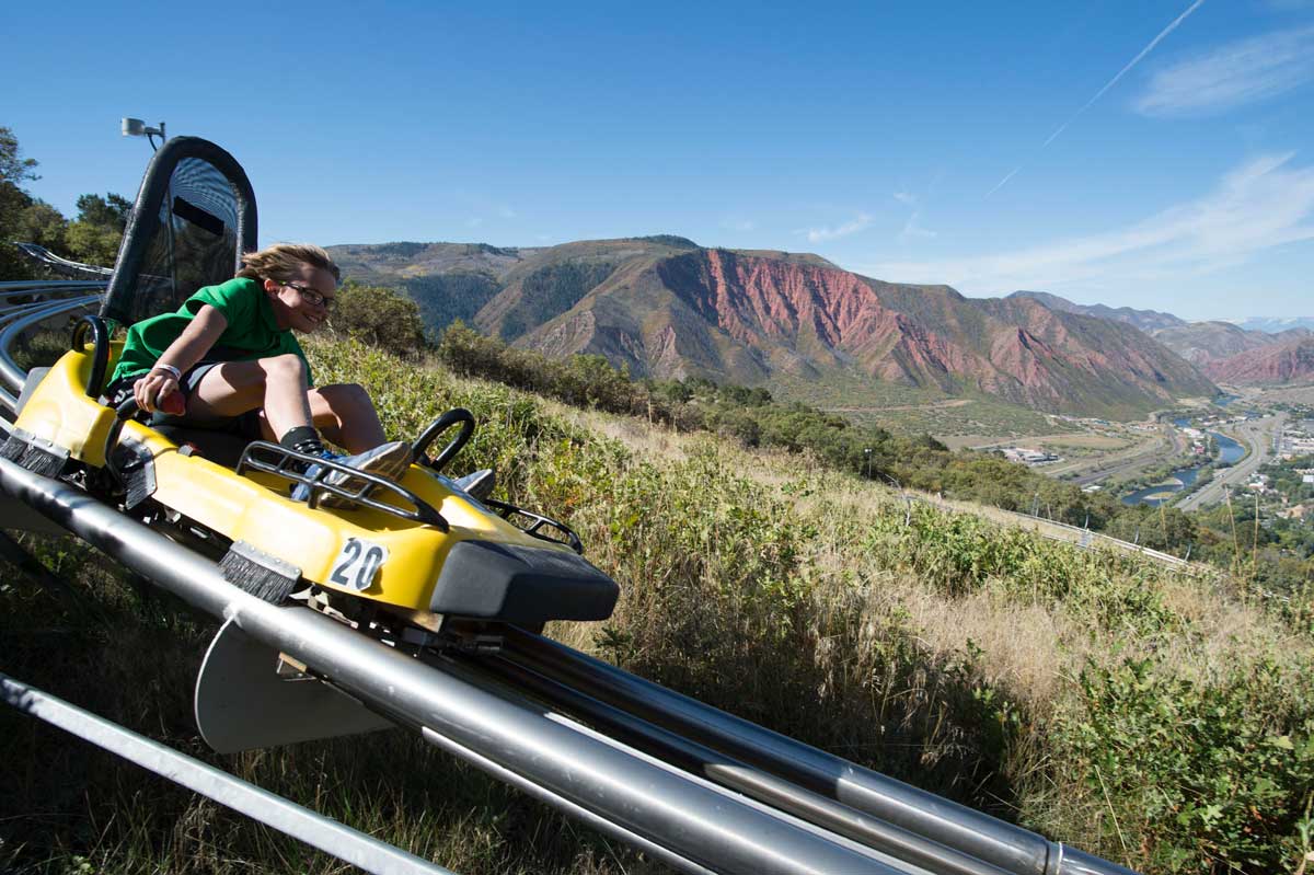 Wind whips through the hair of a child speeding down a mountain in a yellow Alpine Coaster car at Glenwood Caverns Adventure Park.