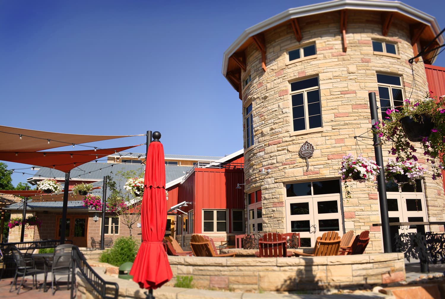 A cylindrical stone building at Odell Brewing Company in Fort Collins with red umbrellas in the foreground