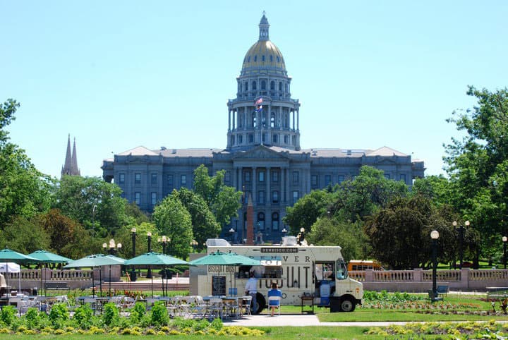 The Denver Biscuit Bus food truck is parked in front of the towering Colorado State Capitol building on a sunny summer day