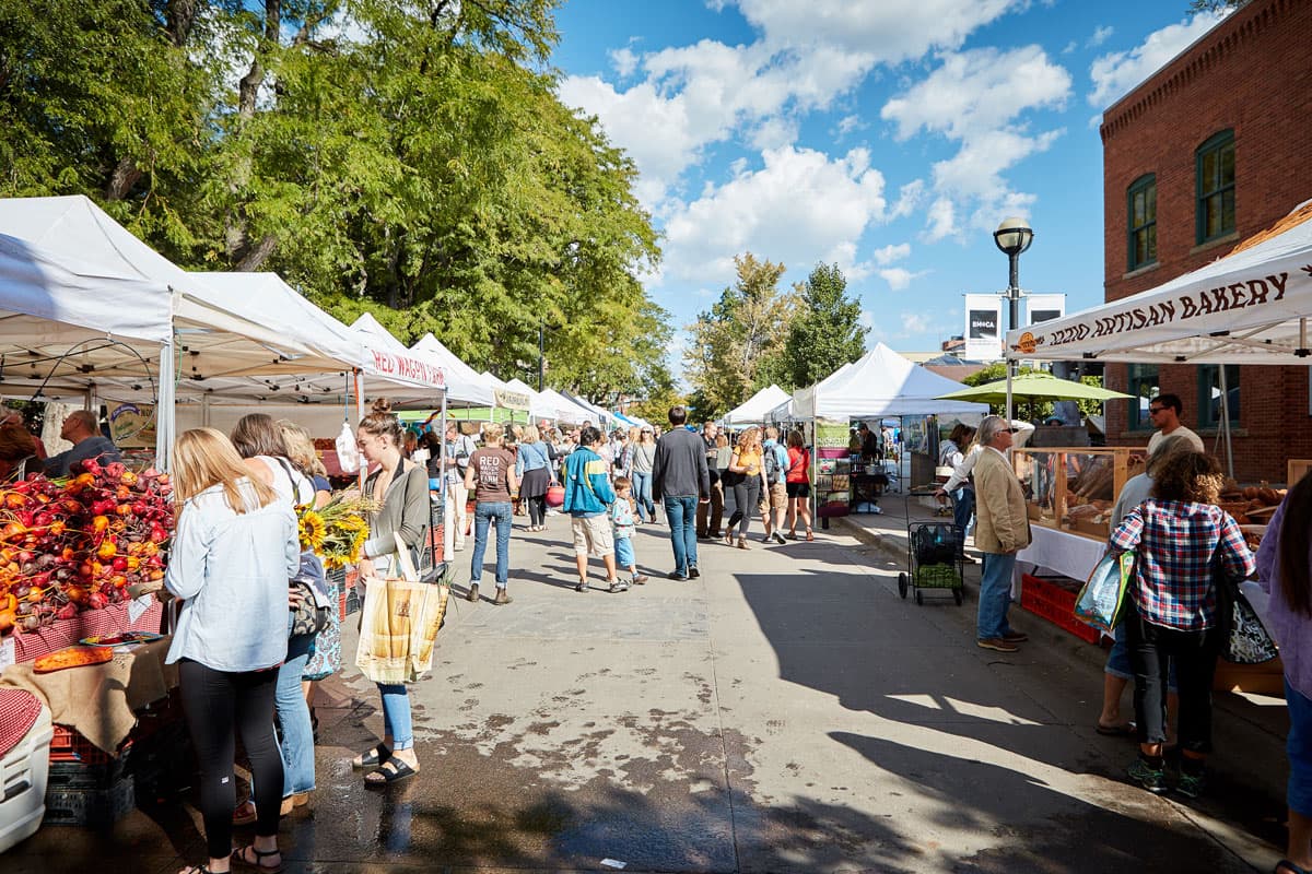 People walking from stand to stand at the Boulder Farmers' Market on a sunny day