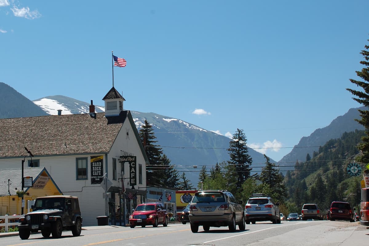 An old white building with a flag on top is on a quiet street with mountains in the background inEmpire, Colorado