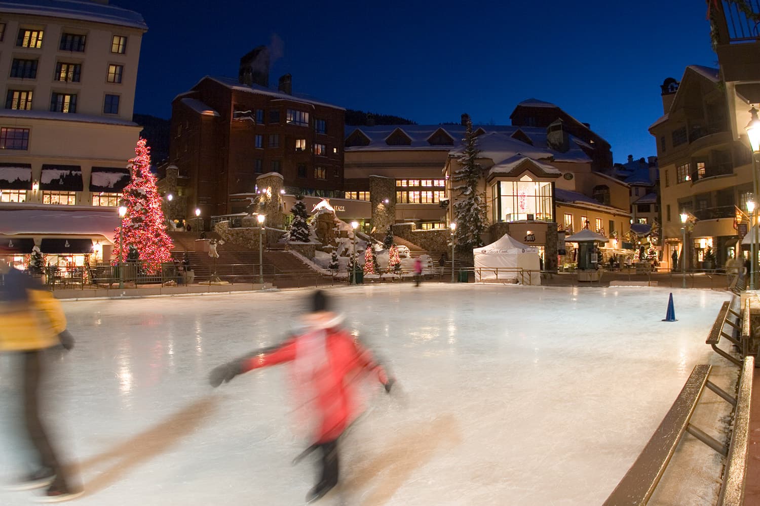 It's nighttime and the ice rink at Beaver Creek Village in Colorado is lit up for evening skaters. A nearby evergreen street is set with red lights.