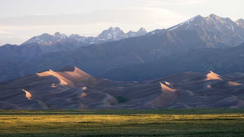 Green prairie lands, wavy sand dunes and towering, snow-capped mountains showcase the diverse environments of the Great Sand Dunes National Park and Preserve in Colorado.