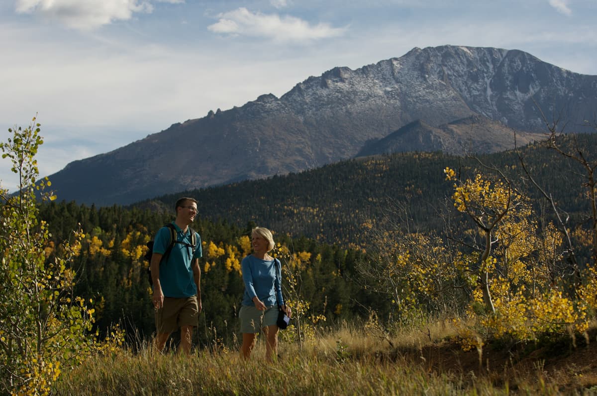 Two people in blue shirts hike through tall grasses amid changing fall foliage near Colorado Springs, Colorado.