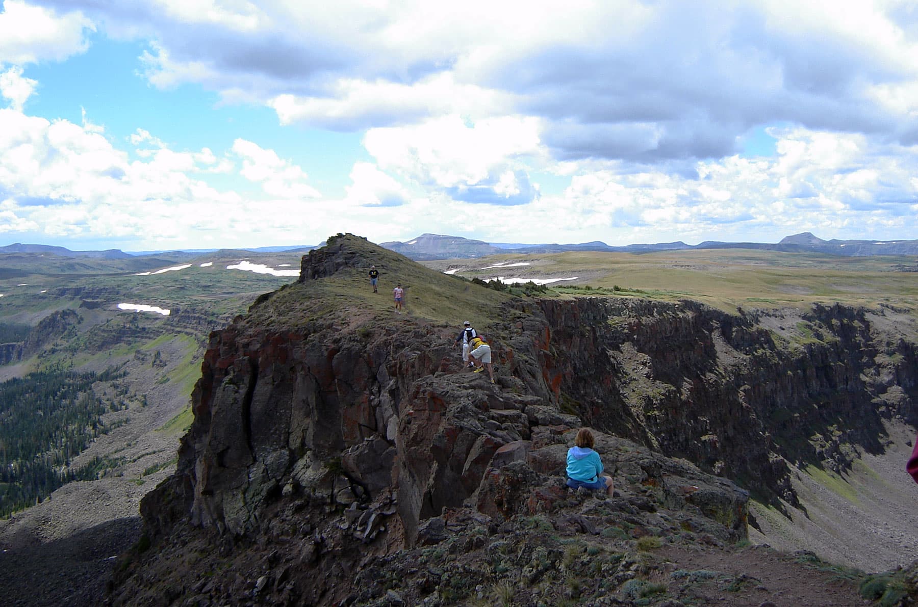 A person in a yellow, long- sleeve shirt holds up their arms in celebration. They stand on the other end of a long, thin and rocky path near Yampa Colorado.