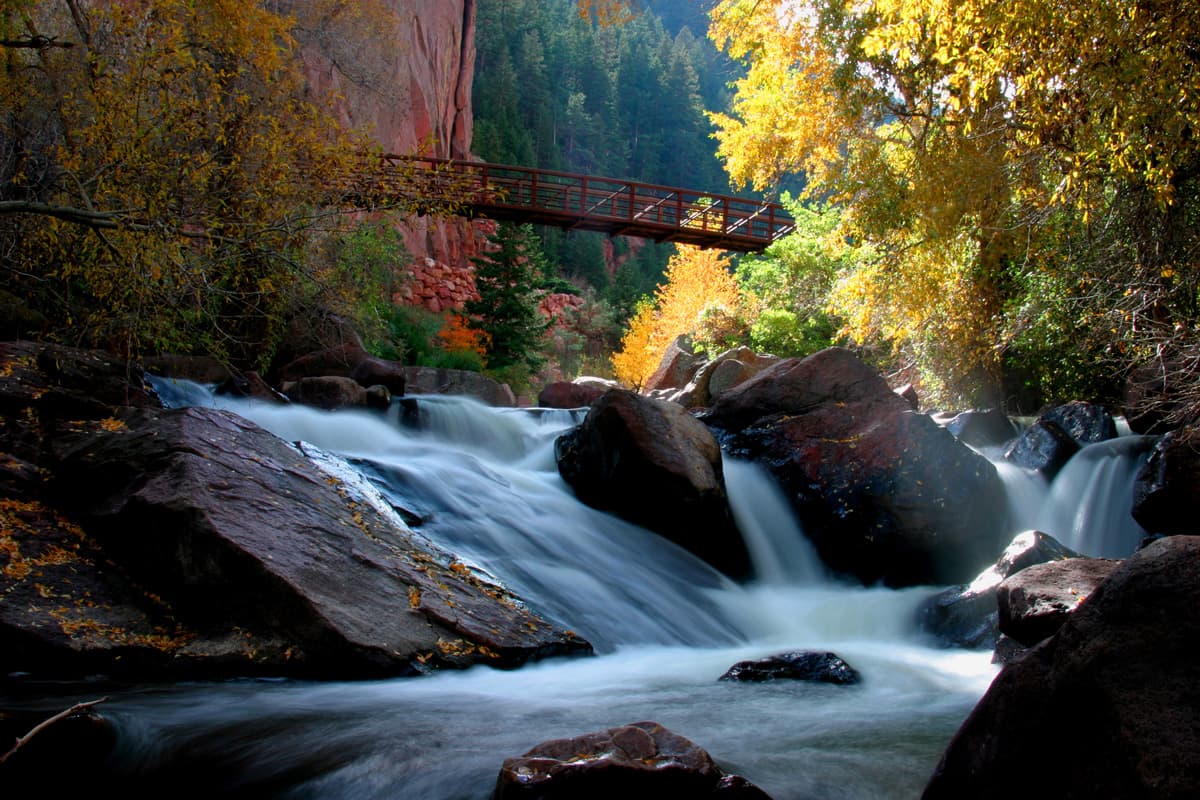 A bridge crosses high above waters cascading down piles of rocks at the Eldorado Canyon State Park in Colorado.