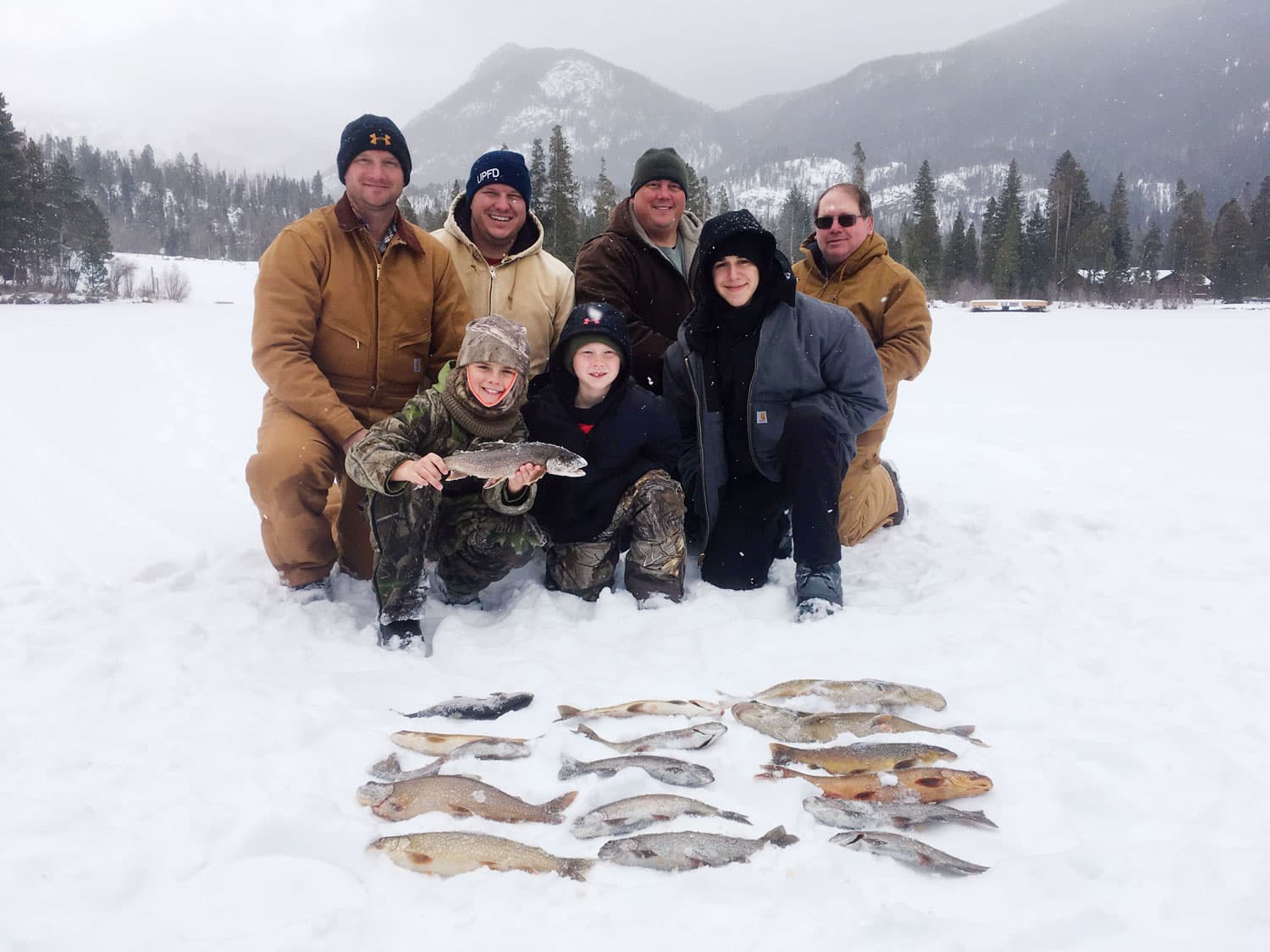 There's a layer of snow on the ground and the surrounding Colorado mountain forest. Amid the snow a family poses with their catch of more than a dozen fish.