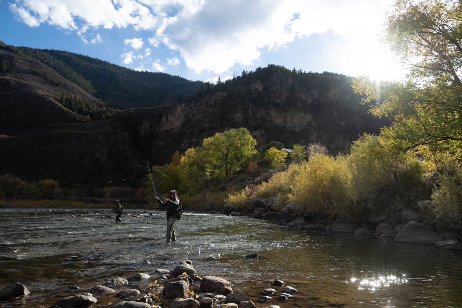 Two anglers stand in the rocky shallows of the Roaring Fork River in Colorado and cast their long wispy lines as they fly-fish.