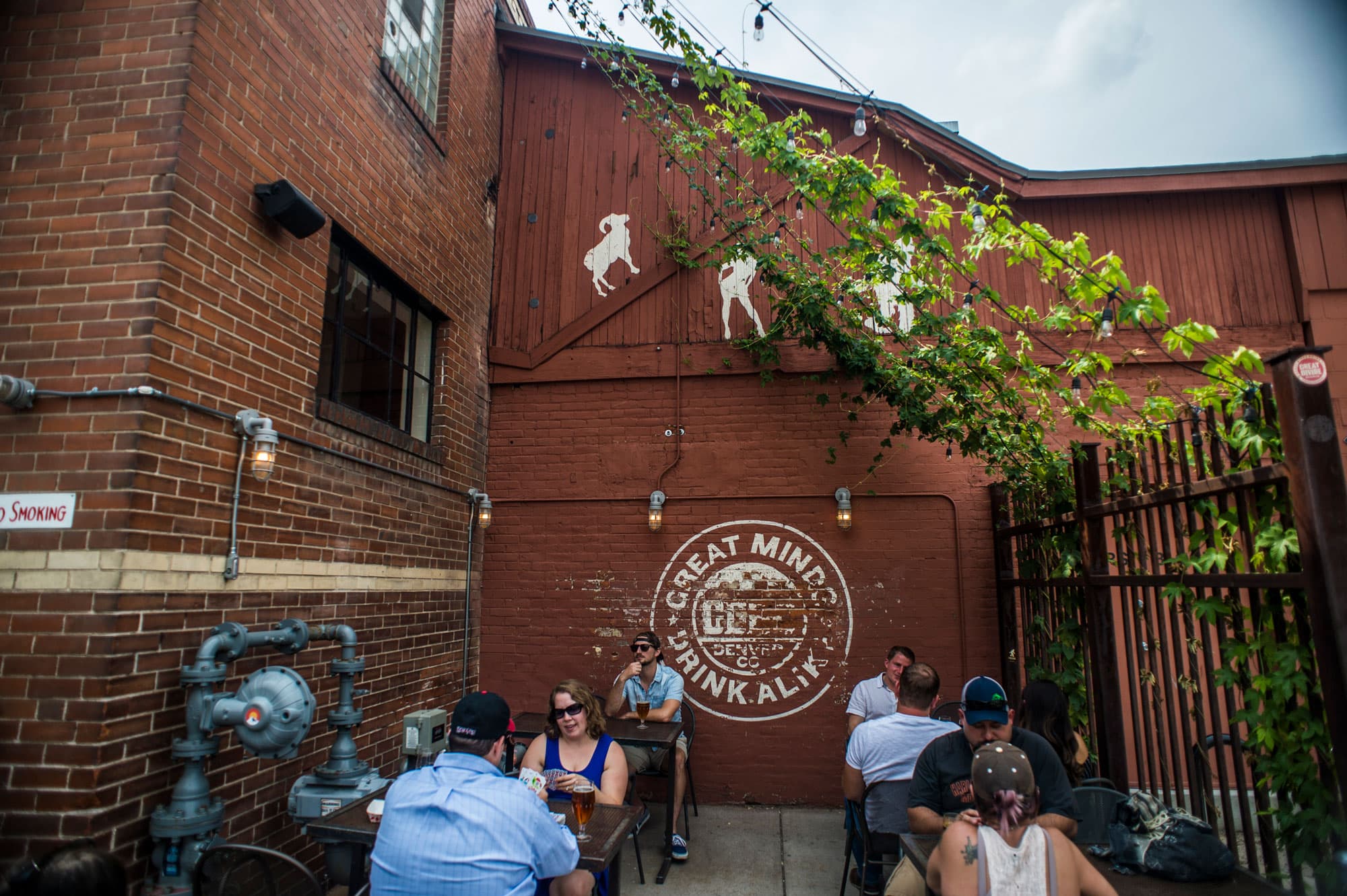 People sit at tables in an outdoor patio space outside a red-brick building in Denver, Colorado.