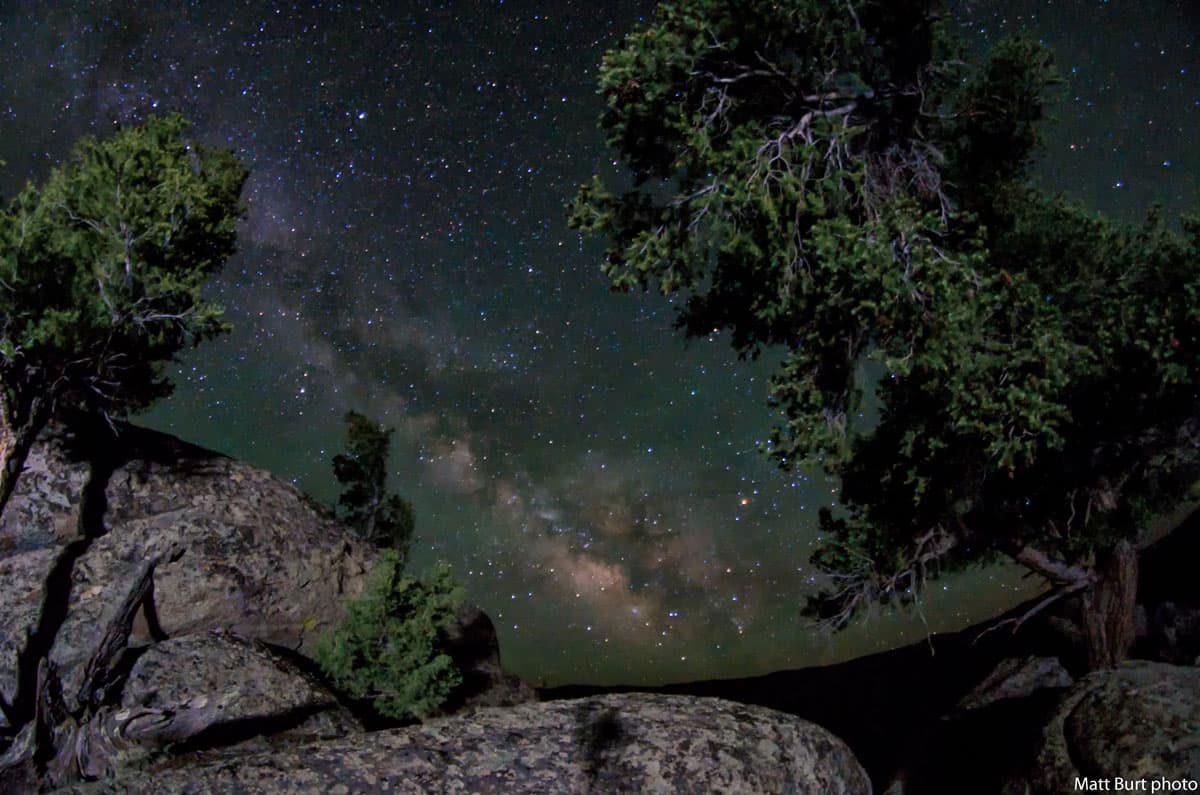 The Milky Way in Gunnison sits above evergreen trees and rocky outcroppings.