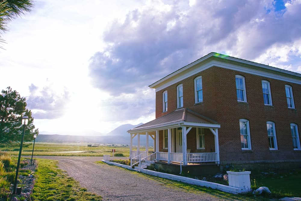 A square, two-story, red-brick building with a small white porch sits on a dirt road with street lanterns near Salida, Colorado.