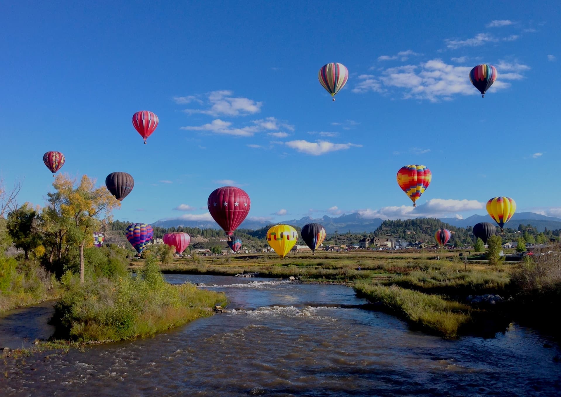 Several colorful hot-air balloons float above a body of water in Pagosa Springs Colorado