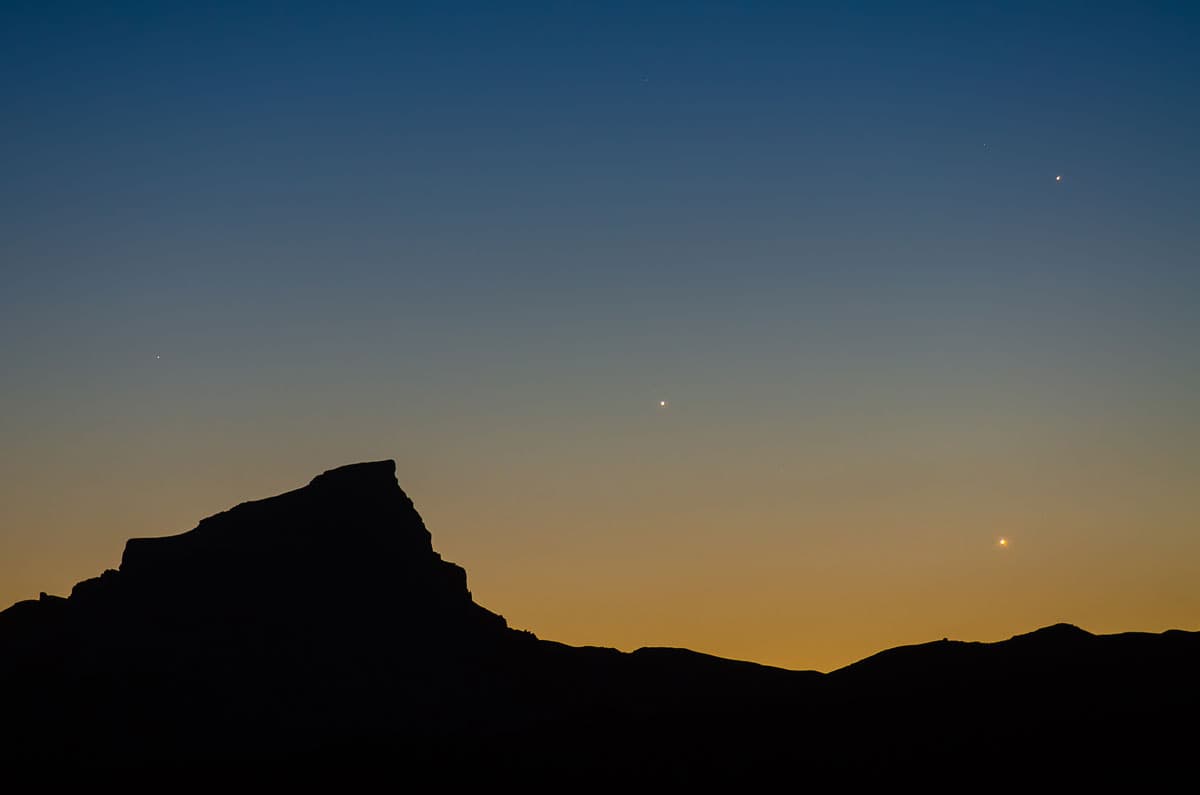 A rocky outcropping sits in the foreground under a dusk sky that's blue at the top and orange toward the bottom.