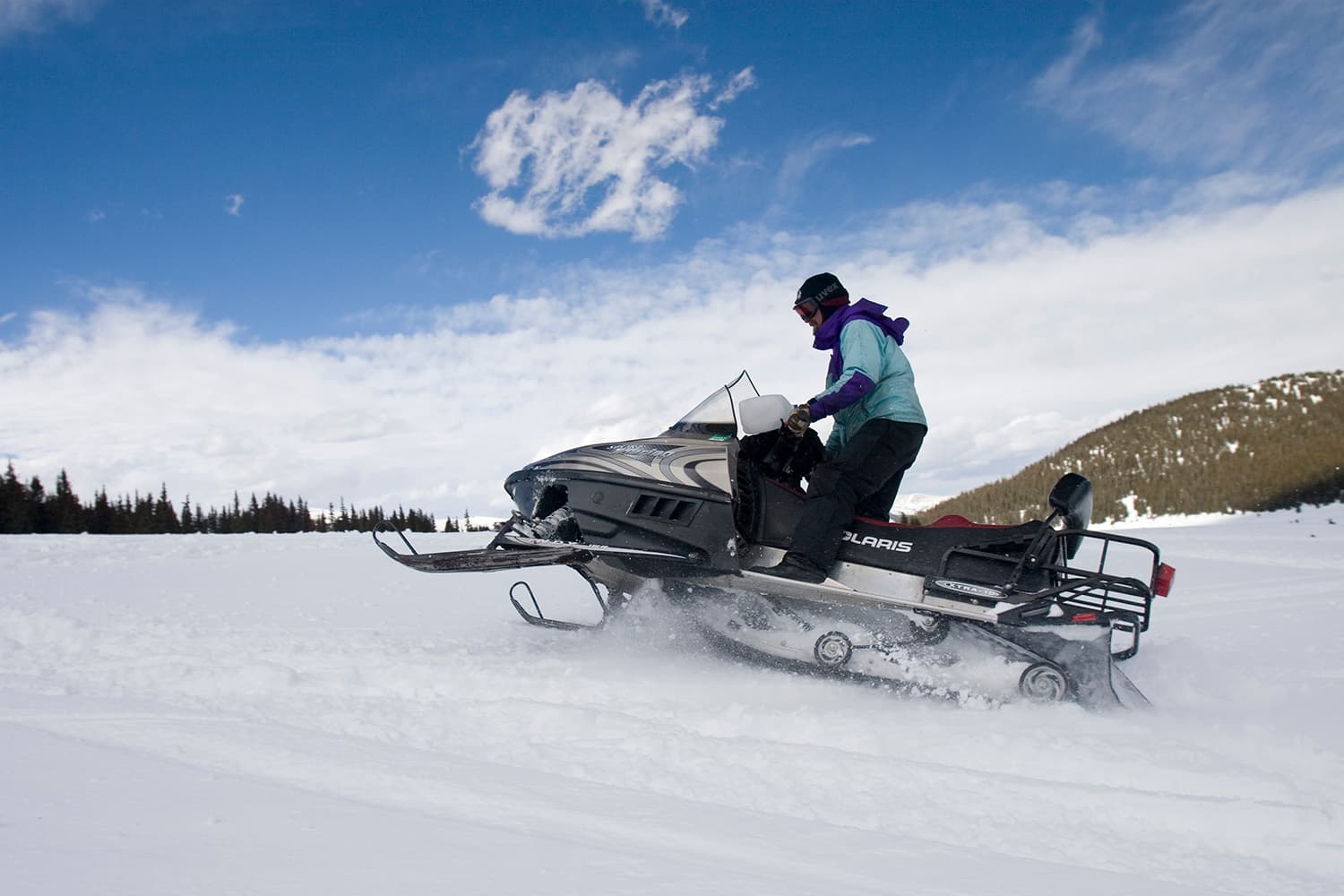 A person on a snowmobile jumps over snow bumps under a blue sky