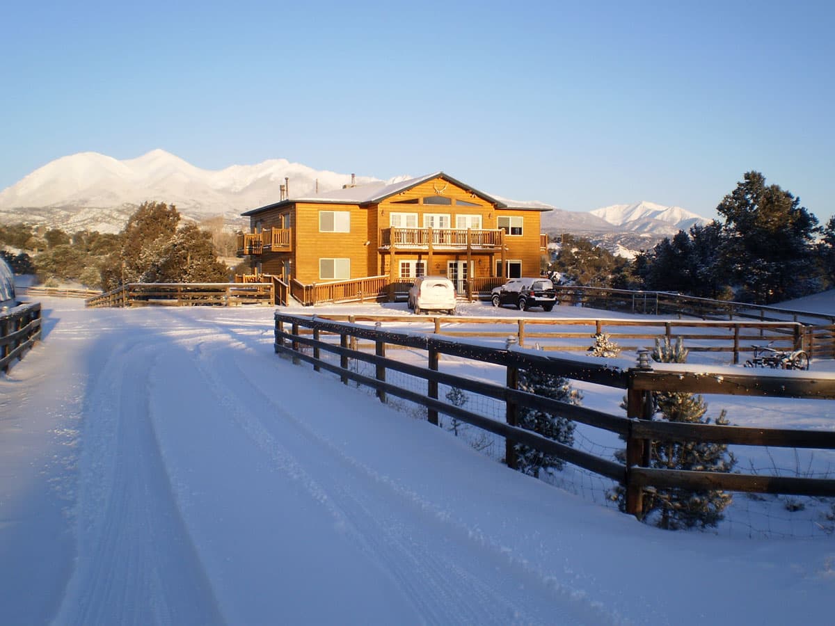 Two SUVs are parked outside a log lodge that features multiple balconies and large windows near Salida, Colorado. Behind it are tall, white mountains.
