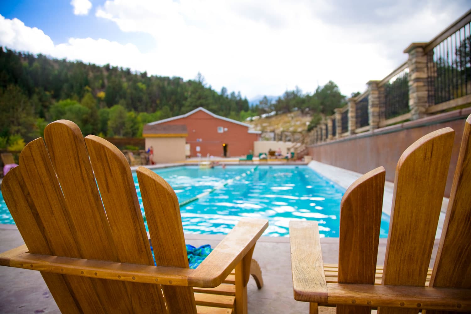 Two light-wood Adirondack chairs sit in front of a blue pool of water at the Mount Princeton Hot Springs Resort in Nathrop, Colorado.