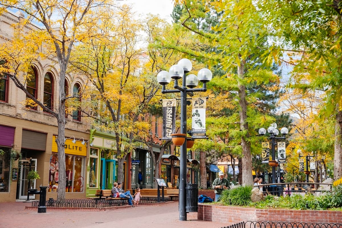 A line of shops on Pearl Street in Boulder with a green tree and street lamp in the foreground