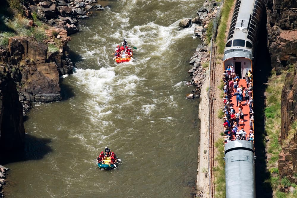 An aerial view of two rafts filled with paddlers passing by a train on the banks of the river