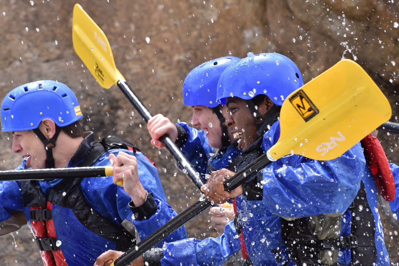 A close up view of three rafters wearing blue helmets, blue waterproof jackets and carrying yellow paddles