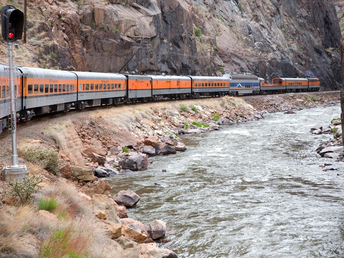 An orange train winds along the rushing Royal Gorege Rive on The Royal Gorge Route