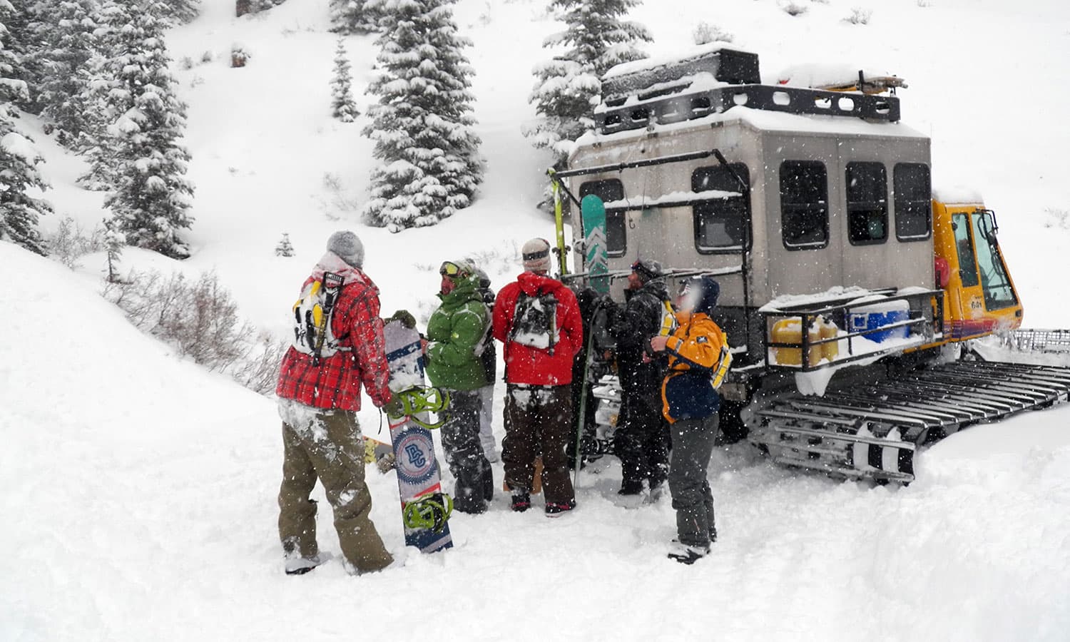 A group of snowboarders gather their equipment from a small gray snowcat with a yellow cab on a mountain near Purgatory, Colorado.