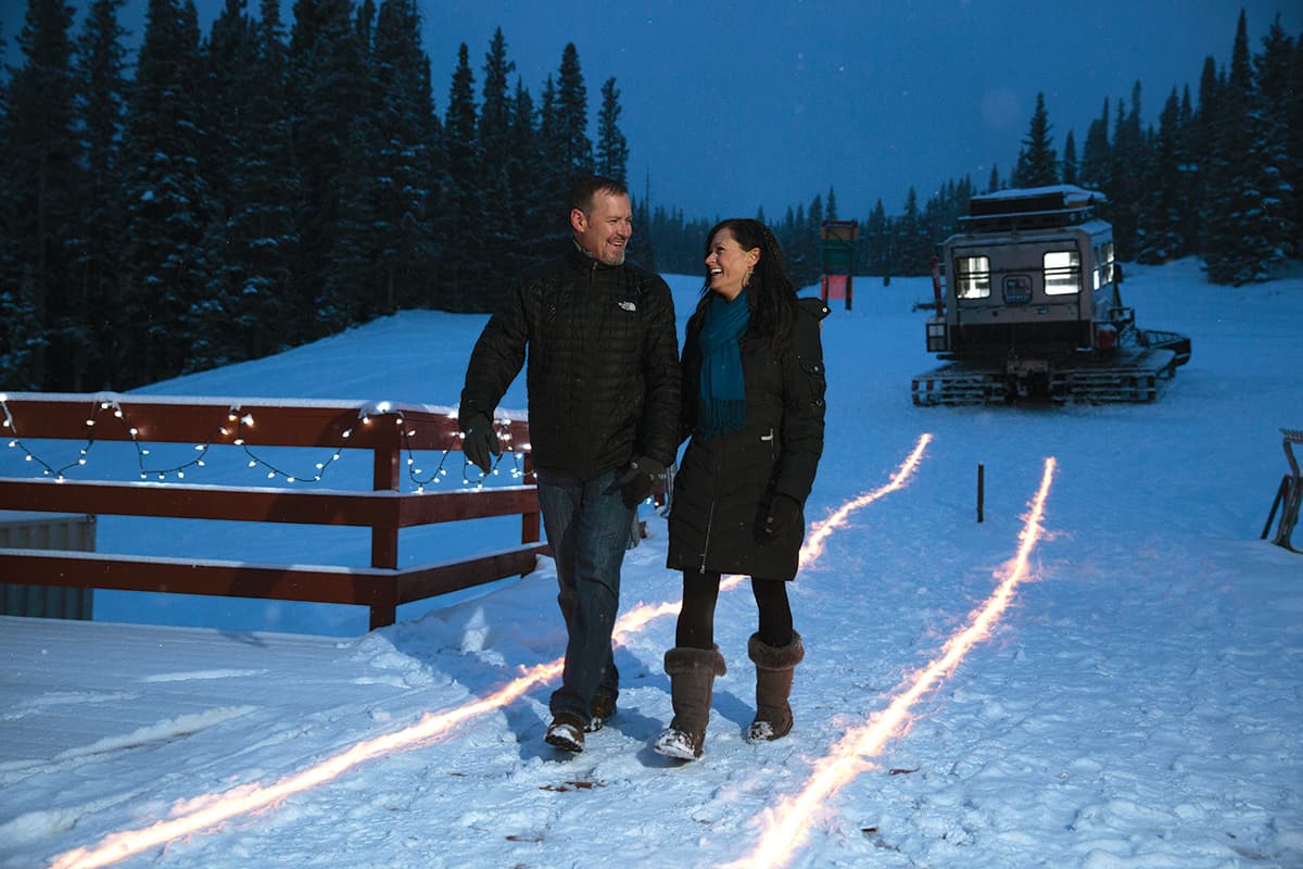 A couple in black clothing walks through away from a snowcat in Colorado.