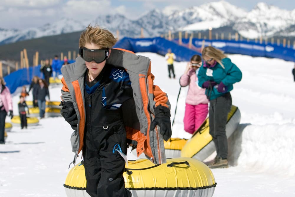 Kids pull snow tubes toward a lift with snowy mountains in the background