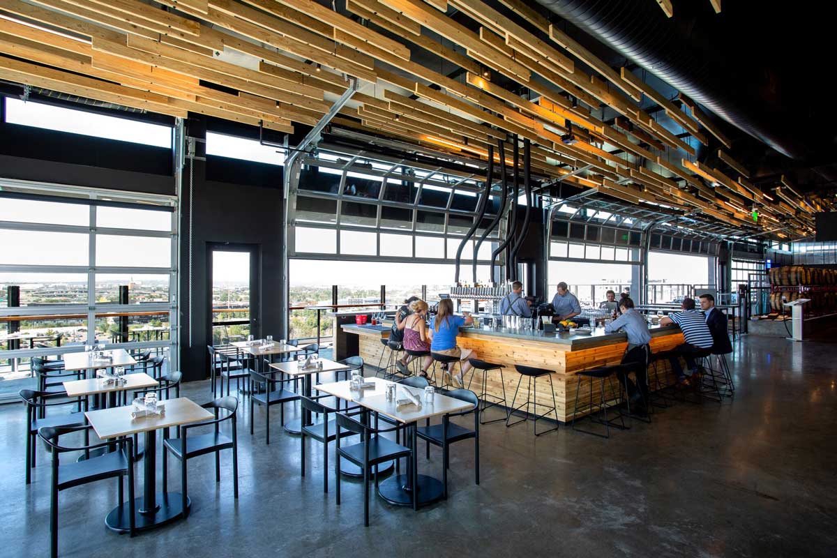 Guests sit around a backlit wooden bar with a black top at The Source Hotel's rooftop restaurant in Denver, Colorado.