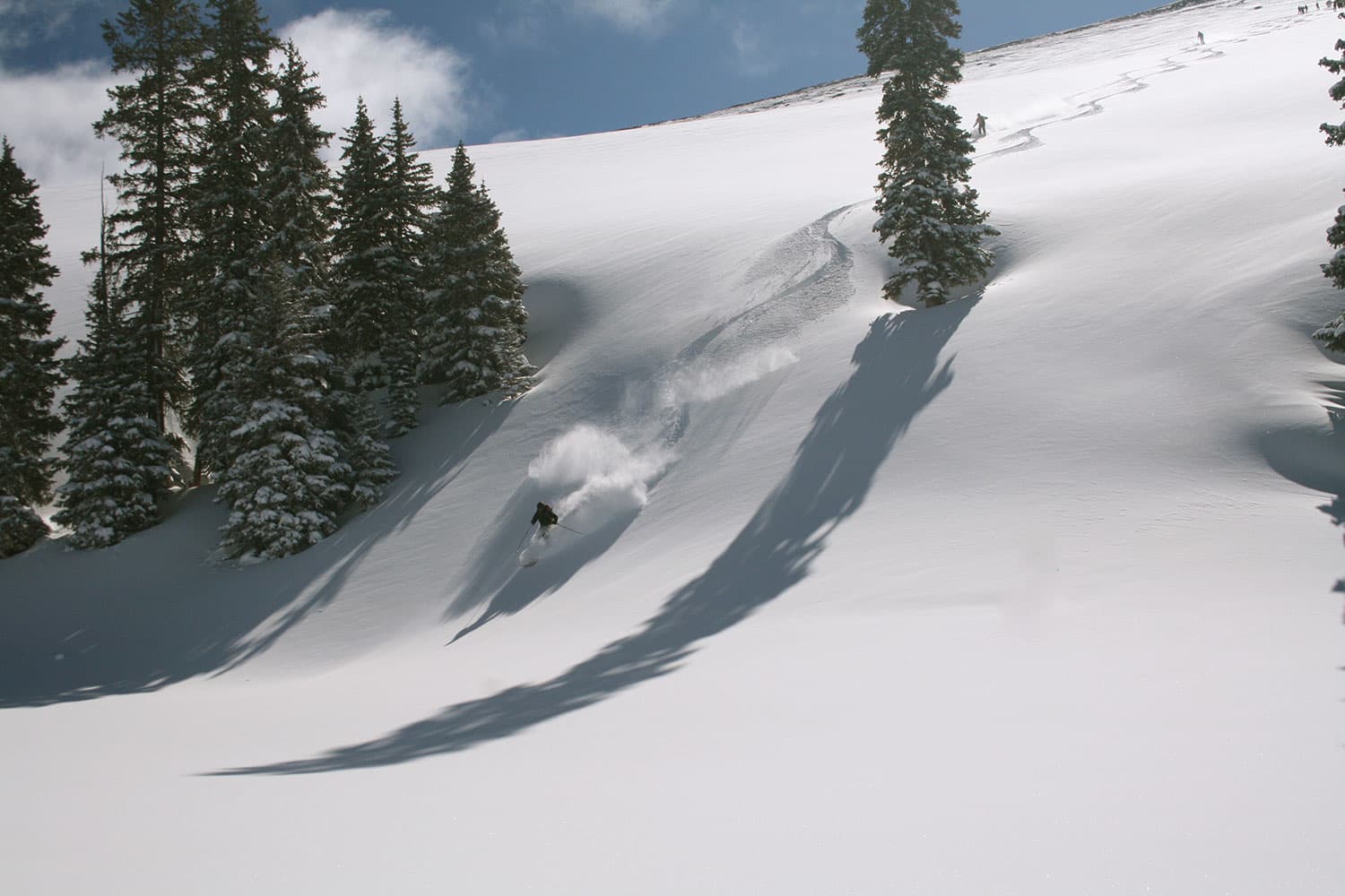 A skier makes the first set of tracks and leaves behind clouds of powder on an untouched snowy slope near Vail, Colorado.