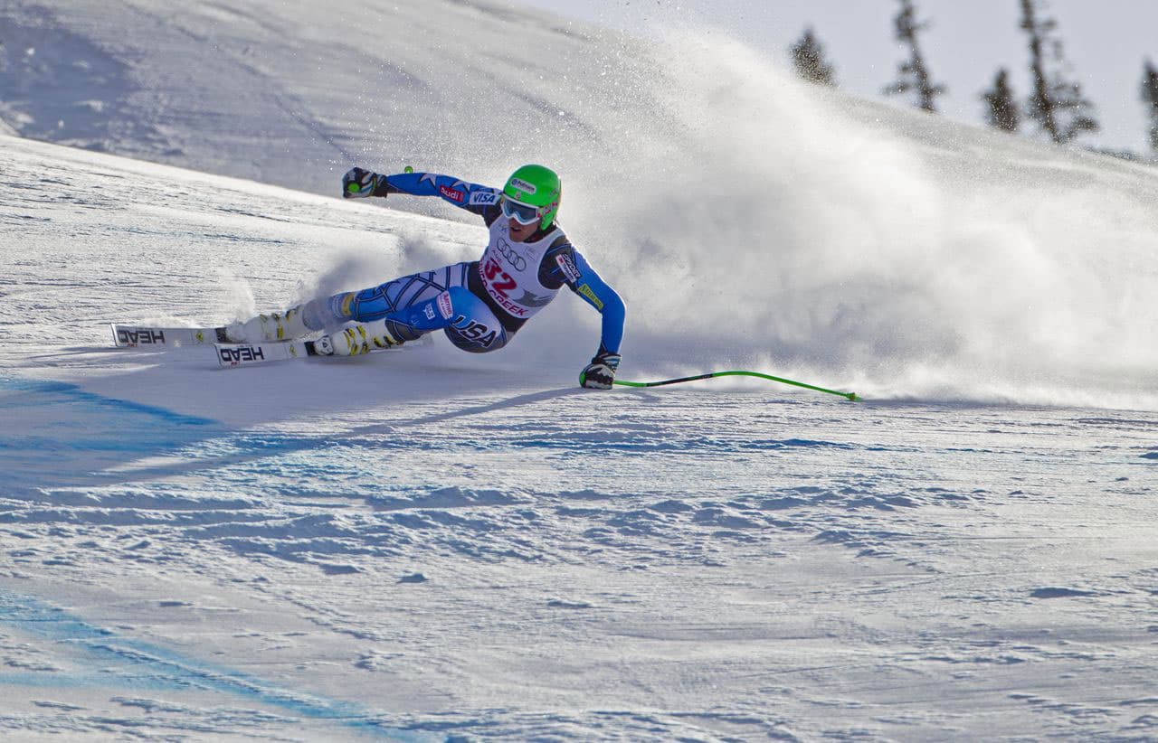 A competitive ski athlete wears a neon green helmet and stirs up fresh snowy powder as they race down the white mountain slope at Beaver Creek Resort in Colorado.