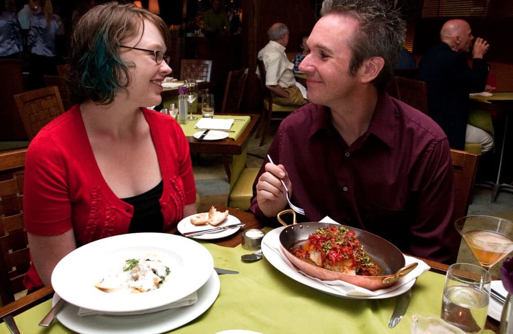 A couple smiles at each other lovingly at a table of food at Summit in Colorado Springs
