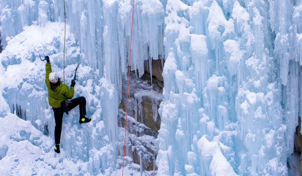 A climber in a yellow-green jacket and white helmet uses picks to help them scale a frozen, icy waterfall near Ouray, Colorado.