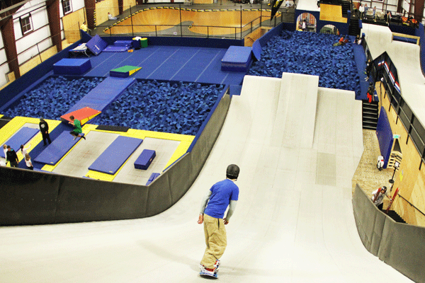 A man glides down a slope into a foam pit at an indoor snowboard park
