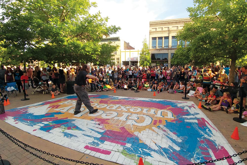 In Greeley, Colorado, a person stands in a roped off area and demonstrates a firey object to the surrounding audience.