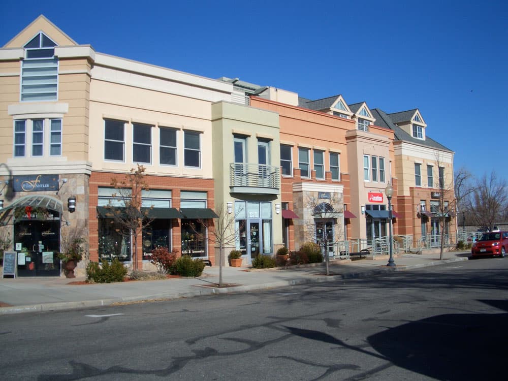 Two story boutiques and shops in historic downtown Louisville on a street with one car and leafless trees.
