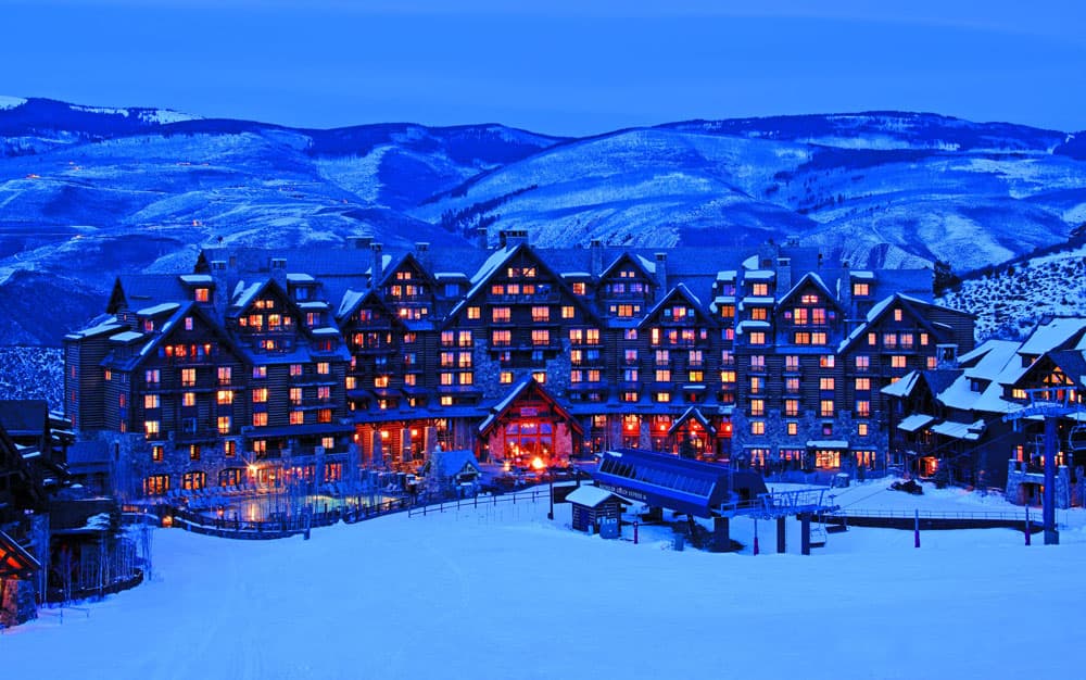 A massive lodge sits at the base of a snowy mountain in Beaver Creek, Colorado. In front of the lodge is an outdoor pool space, a firepit and a ski lift.