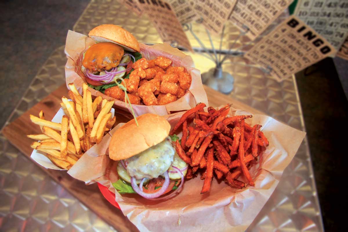 A platter of large sandwiches, french fries and tater tots on a restaurant table