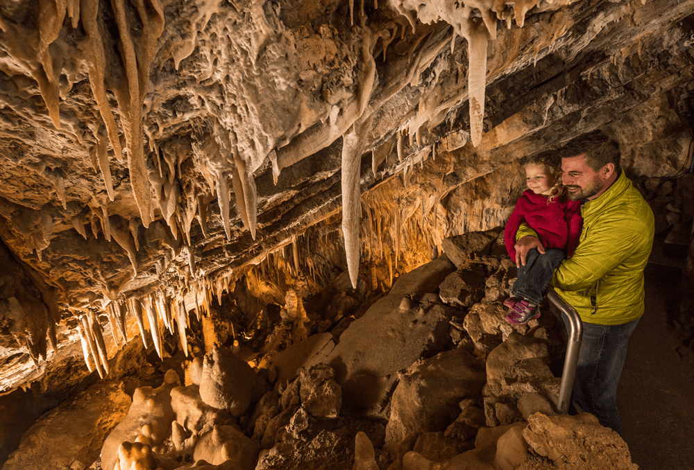 A man holds up a child to look at formations inside a cave