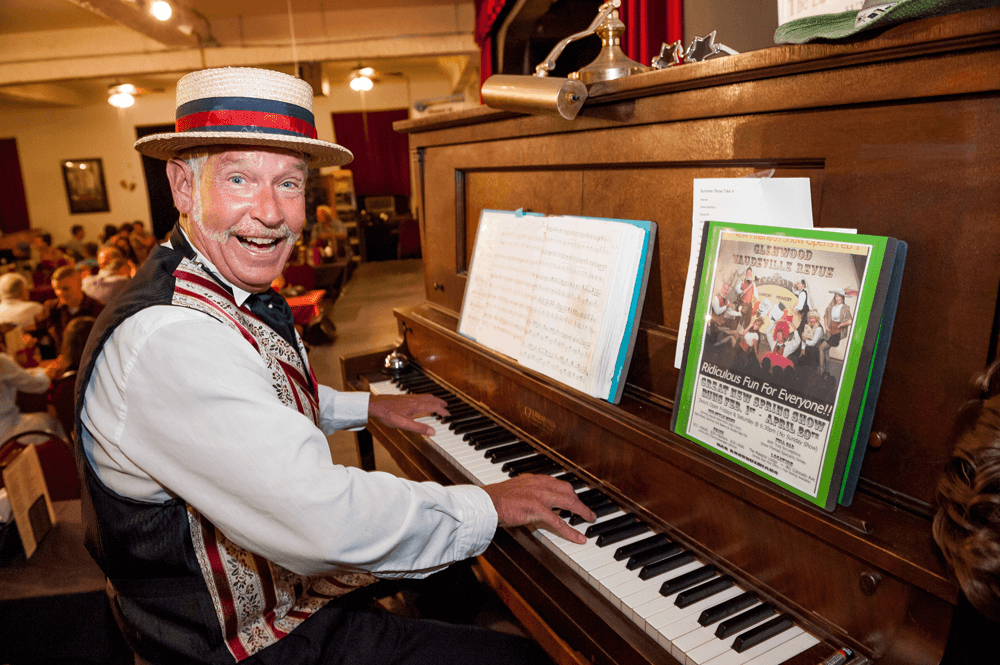A man in a vaudeville costume smiles while playing the piano