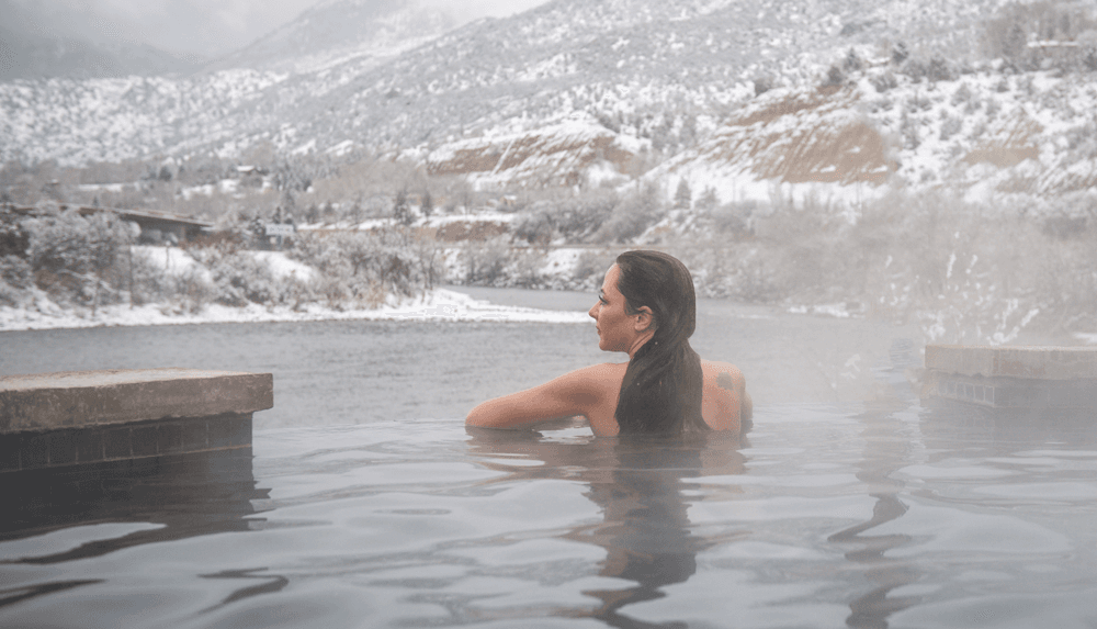 A woman soaks in hot springs while looking out over snowy mountains