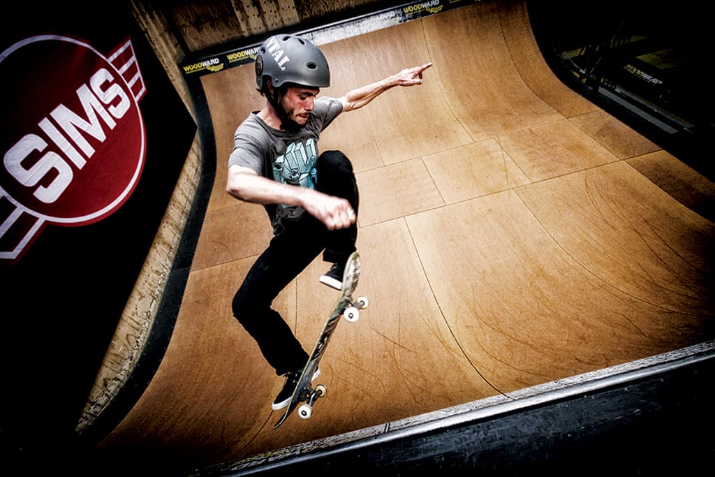 A skateboarder on an indoor half pipe ollies into the air